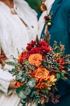 Crop blurred just married couple in elegant clothes hugging and holding beautiful bouquet of fresh colorful flowers in composition with green and brown herbs