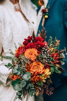 Crop blurred just married couple in elegant clothes hugging and holding beautiful bouquet of fresh colorful flowers in composition with green and brown herbs