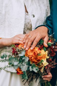 Crop blurred just married couple in elegant clothes hugging and holding beautiful bouquet of fresh colorful flowers in composition with green and brown herbs