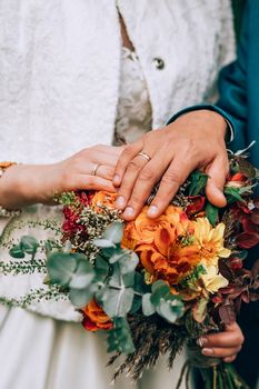 Crop blurred just married couple in elegant clothes hugging and holding beautiful bouquet of fresh colorful flowers in composition with green and brown herbs