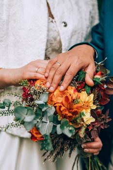 Crop blurred just married couple in elegant clothes hugging and holding beautiful bouquet of fresh colorful flowers in composition with green and brown herbs