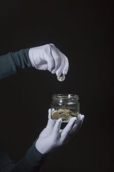 Hand in a white glove throws a coin into a glass jar