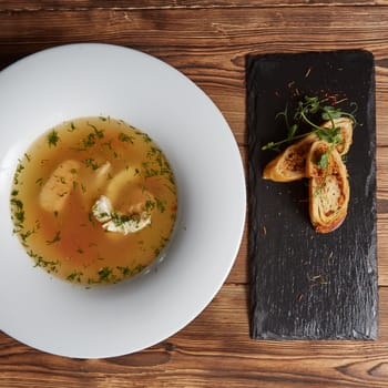 Beautiful presentation of the fish soup in a white plate, with bread on a wooden background, top view.