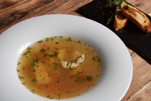 Beautiful presentation of the fish soup in a white plate, with bread on a wooden background, top view.