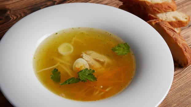 Tasty hot homemade dinner, diet food, healthy delicious meals. Meat broth with chicken meat, egg and parsley in a white bowl, bouillon with croutons.