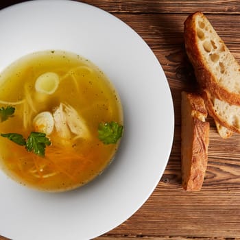 Tasty hot homemade dinner, diet food, healthy delicious meals. Meat broth with chicken meat, egg and parsley in a white bowl, bouillon with croutons.