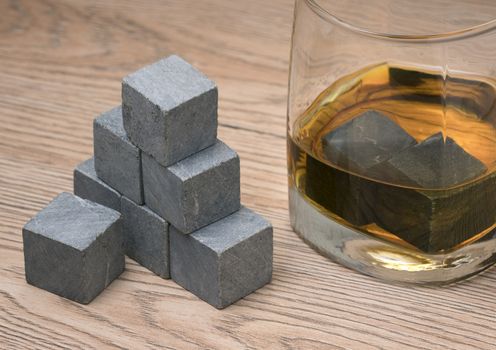 Glass with whiskey and whiskey stones on wooden background