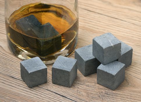 Glass with whiskey and whiskey stones on wooden background