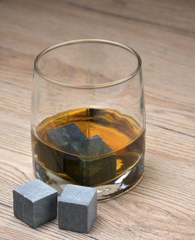 Glass with whiskey and whiskey stones on wooden background
