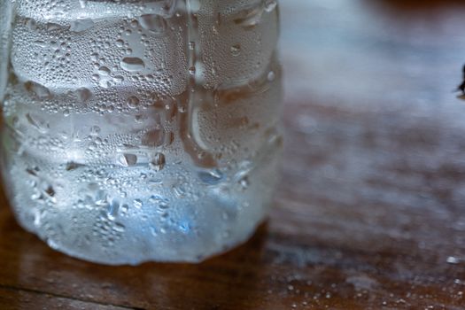 The Clear water drop on cool water bottle on wooden table with blur background