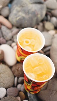 Paper cup with lemonaide on the background of stones, pebble beach. Beach Vacation Concept