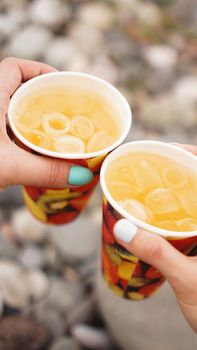 male hand holding paper cup with lemonaide on the background of stones, pebble beach. Beach Vacation Concept