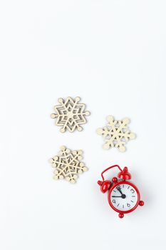 Simple Christmas composition. Small analog red clock, wooden snowflakes on white background. Minimal style flat lay, for social media. Top view. Celebration concept.