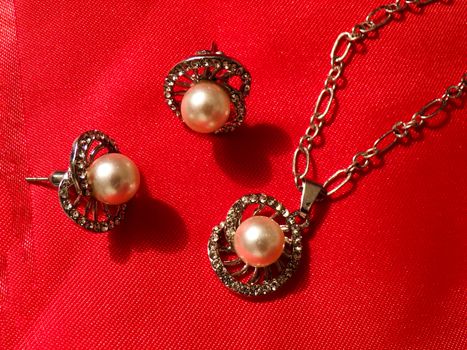 Beautiful earrings and pendant on a chain. Set of jewelry made of silver on a silk red fabric close up. Jewelry made of precious metals and stones.