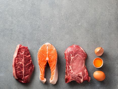 Carnivore or keto diet concept. Raw ingredients for zero carb or low carb diet - rib eye, salmon steak, pork, egg on gray stone background. Top view or flat lay. Copy space top.