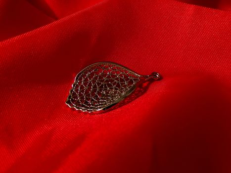 Jewelry on red silk fabric. Beautiful female pendant made of 925 sterling silver. Necklace in the form of a petal close-up.