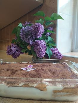 Tiramisu cake in glass blouse. Magnolia and lilac decoration.