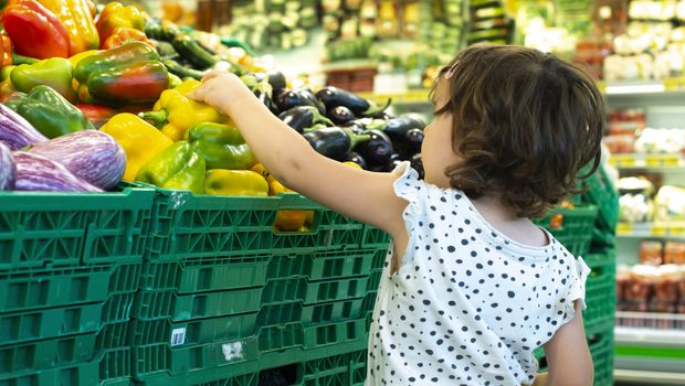 Child shopping peppers in supermarket. Concept for buying fruits and vegetables in hypermarket. Little girl hold shopping basket.