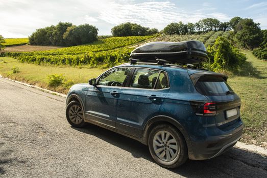 Tourist car in vineyards. Countryside and car with luggage box on top. Rural tourism concept with car and wine grapes on background. Travel concept.