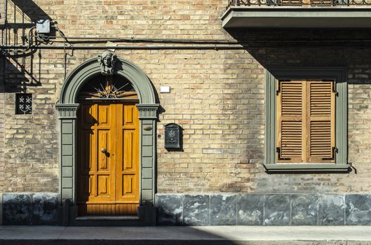 Old typical italian wooden door. Italian house. Ancient house facade. Sunlight. Round door arch. Stone build house. Wrought iron door handles.