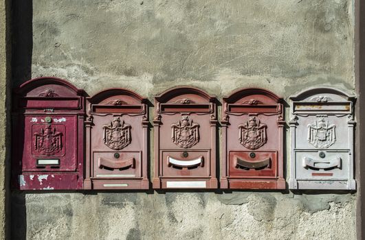 Old vintage mailboxes in Italy. Metal red mailboxes on grey facade. Hard sunlight. Empty plates. Italian house wall. Vintage mail correspondence concept.