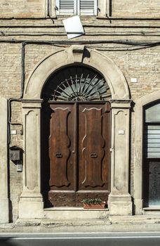 Old typical italian wooden door. Italian house. Ancient house facade. Sunlight. Round door arch. Stone build house. Wrought iron door handles.