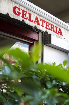 Text gelateria on sunblind. Italian ice cream. Facade on ice cream shop. Green foliage in front of cafe and ice cream shop.