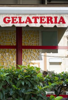 Text gelateria on sunblind. Italian ice cream. Facade on ice cream shop. Green foliage in front of cafe and ice cream shop.