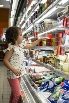 Little girl buying yogurt in supermarket. Child in supermarket select products from store showcase. Concept for children selecting milk products in shop.