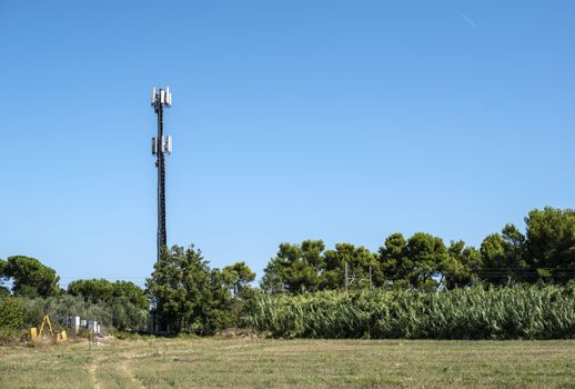 Telecommunication 5G transmitters. GSM antenna on blue sky. Antenna in the nature. New 5G technology concept. Green foliage and trees.