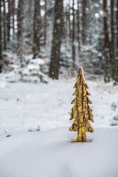 Wooden shaped pine tree in the snow in forest. Fir tree shape and shiny paint. Snowing in the forest. Gold colors