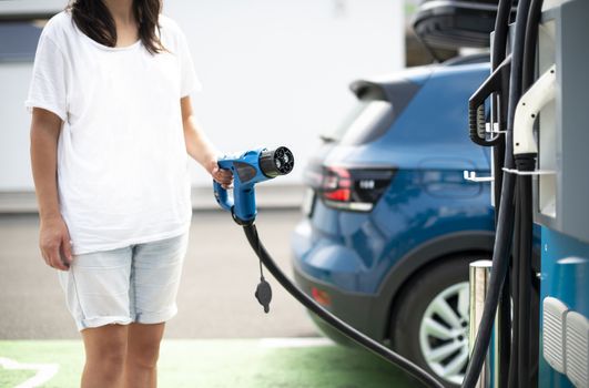 Woman charge her Electric car on gas station. Blue car and electric plug for charging. Ecology fuell concept.