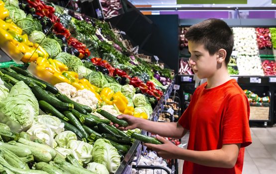 Child selecting vegetables on shelf in supermarket. Cabbage, zucchini, pepper and cauliflower.