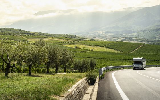 Asphalt road, vineyards and olive trees in countryside. Travel with camper. Wine and food travel concept. Italian agriculture.