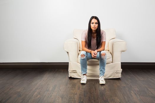 mid-twenties young woman wearing jean with hold on the knees, sitting on a couch