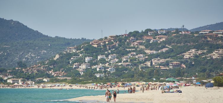 Image of the town of Costa Rei in Sardinia taken from the crowded beach during the daytime.