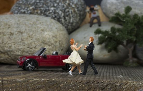 little miniature figures dancing at the wedding near a red cabriolet car toy