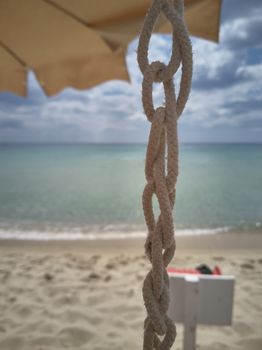 Detail of a knotted and woven sailor cord with the blurred background of the beach and the sea.