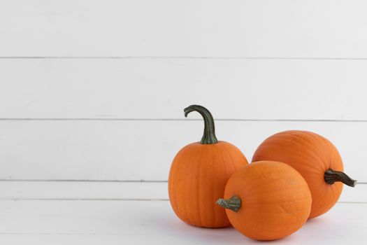 Three orange pumpkins on white wooden background, Halloween concept