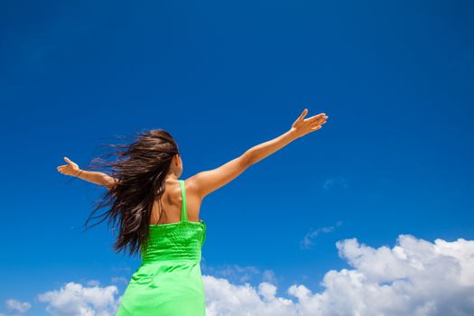 Young woman with raised hands over blue sky background