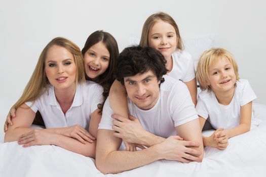 Family of parents and three children in white clothes laying on white background