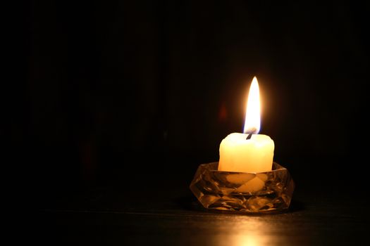 One lighting candle in candlestick against dark background