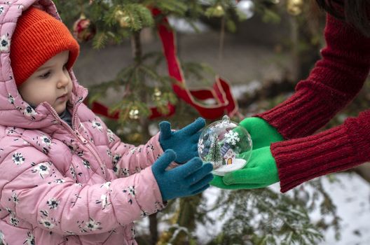 Crystal christmas ball with house and snow inside. Hands with green gloves gives transparent ball to a child.