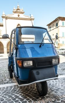 Typical italian farm truck on three wheels. Parked in ancient italian square.