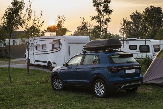 Caravans and campers on green meadow in campsite. Sunrise, rays on campers in the morning. Green grass. Outdoor concept for traveling and res in the nature.