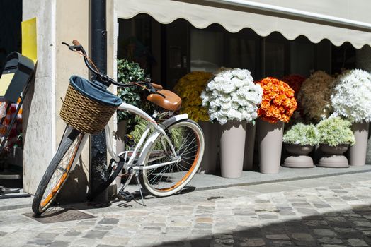 White bike with wicker basket on italian street. Many Pots with flowers on background. Sunny day. Typical italian style.