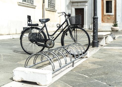 Black bike mounted on a bicycle stand on italian street. 
