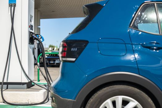 Electric car on gas station. Blue car and electric plug for charging. Ecology green fuels concept.