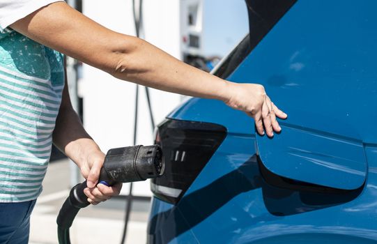 Woman charge her Electric car on gas station. Blue car and electric plug for charging. Ecology fuell concept.