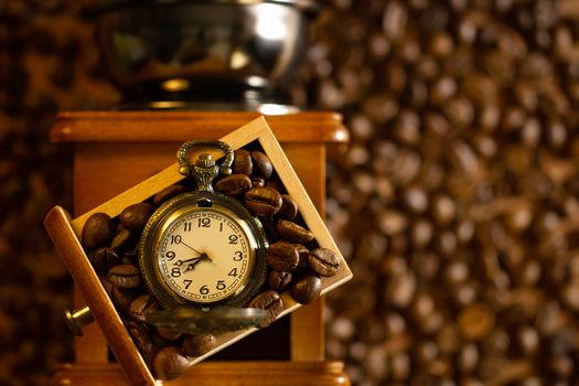 Coffee bean and pocket watch the tray of manual grinder on table. Top view and copy space. Concept of coffee time in morning.